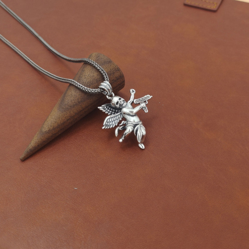 S925 sterling silver armed angel skull pendant on brown textured surface showing scale and oxidized finish detail