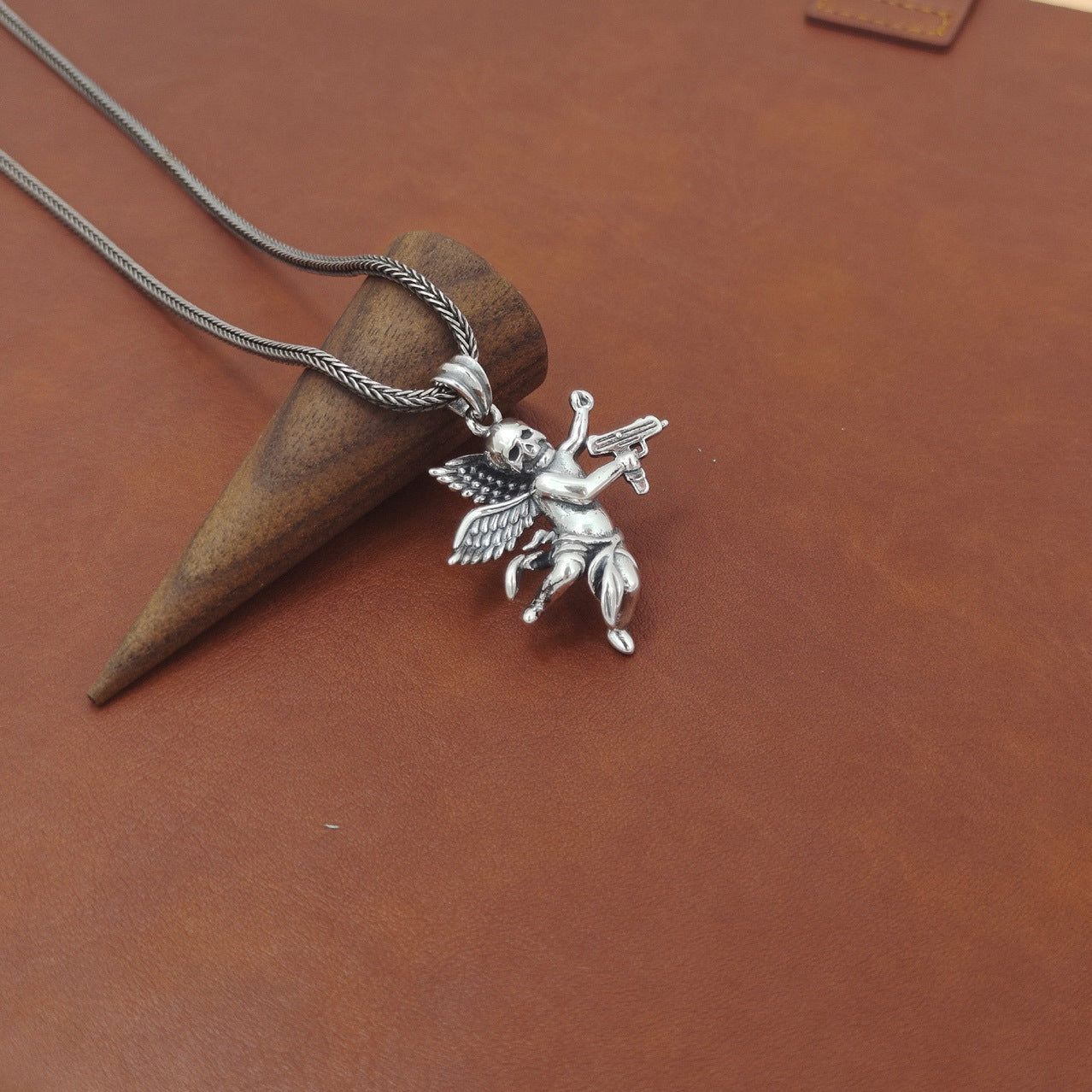 S925 sterling silver armed angel skull pendant on brown textured surface showing scale and oxidized finish detail