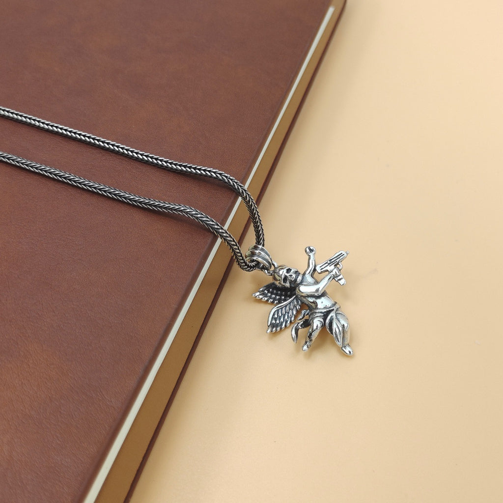 S925 sterling silver armed angel skull pendant on chain displayed on cream surface with book showing everyday styling context