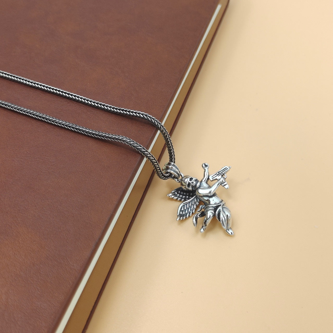 S925 sterling silver armed angel skull pendant on chain displayed on cream surface with book showing everyday styling context