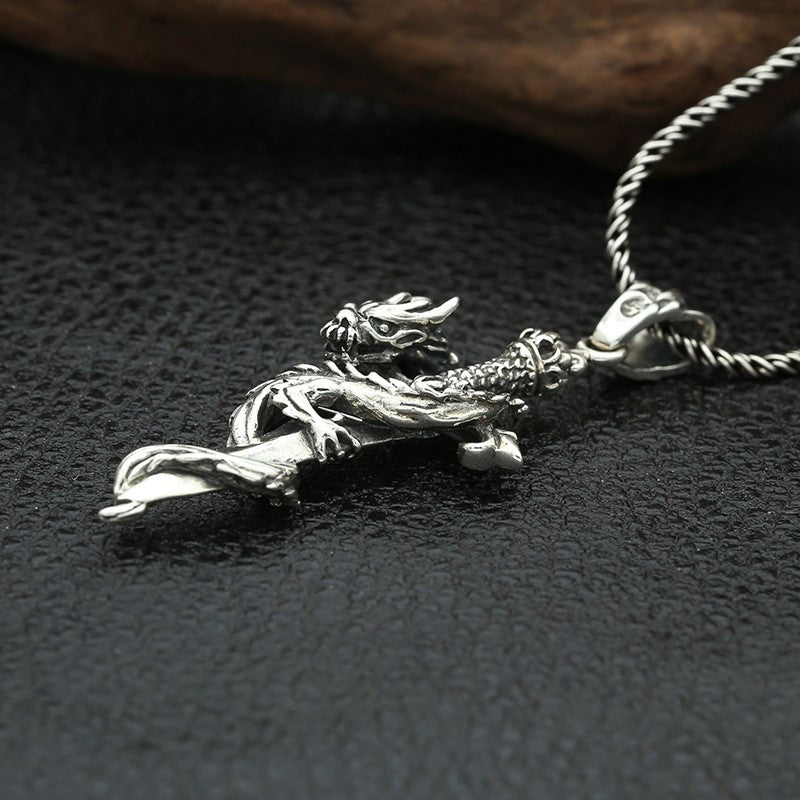 S925 sterling silver cross sword dragon pendant laying on dark surface showing full entwined dragon cross design and oxidized finish