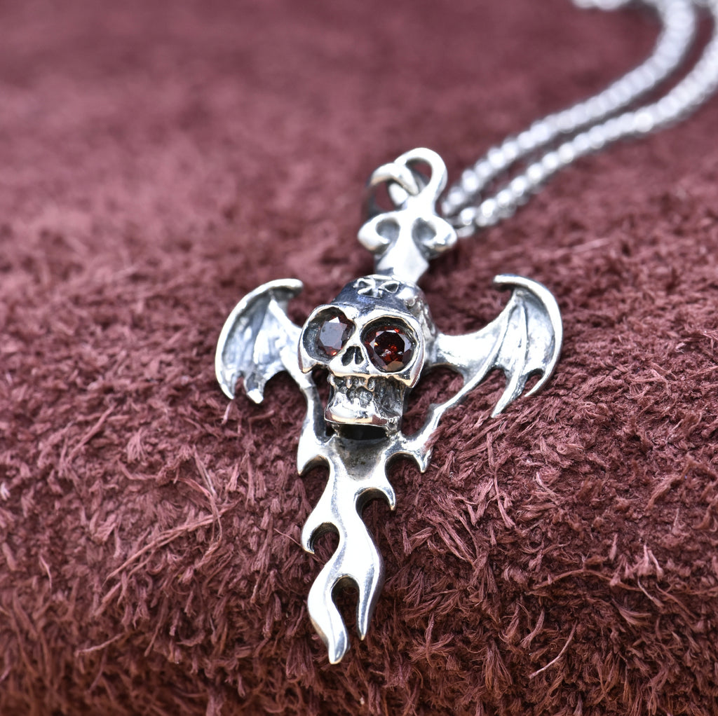 Close-up of S925 sterling silver devil wing skull pendant on purple fabric showing red zircon eyes and oxidized detailing