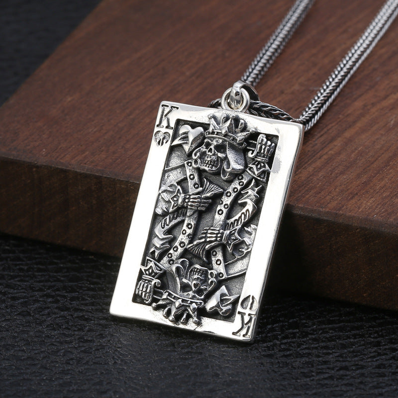 S925 sterling silver king card pendant angled view on wood showing raised skeleton relief, ornate borders and oxidized finish