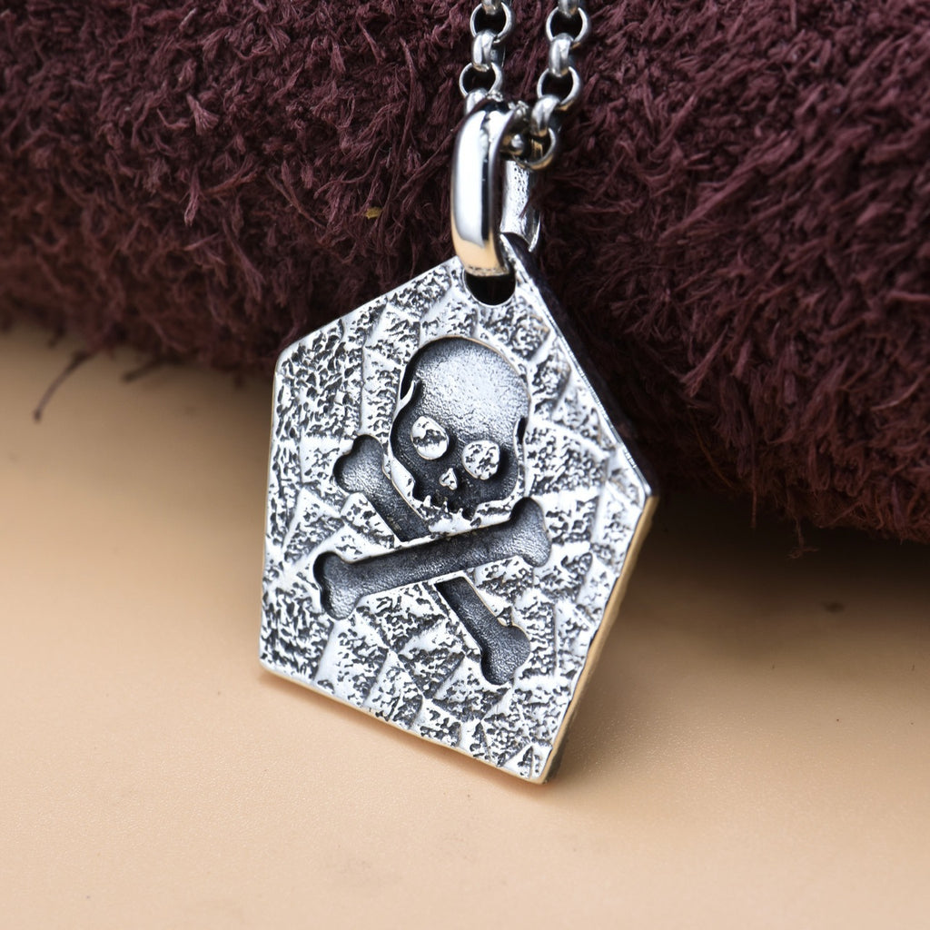 Back view of S925 sterling silver pirate skull pendant on tan surface showing reverse side detail oxidized finish and solid construction