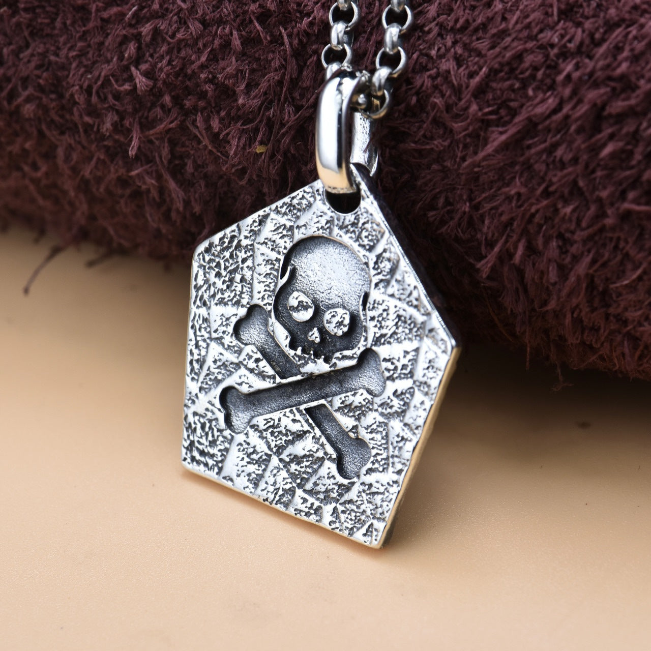 Back view of S925 sterling silver pirate skull pendant on tan surface showing reverse side detail oxidized finish and solid construction