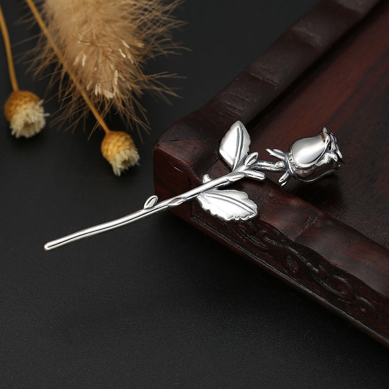 Angled view of S925 sterling silver rose pendant on dark surface showing detailed petals leaves and dimensional craftsmanship