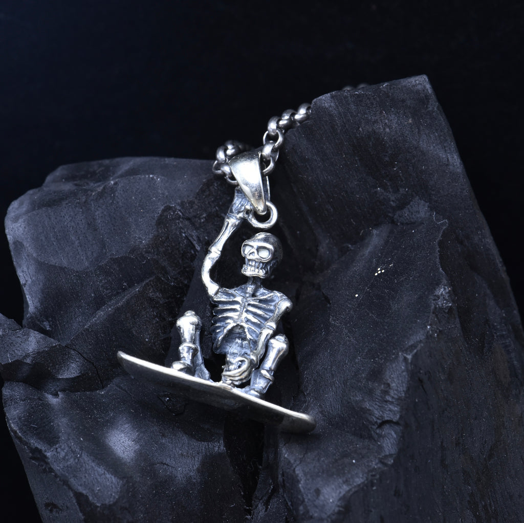 S925 skeleton snowboarder pendant on dark stone showing side profile with ribcage detail and snowboard