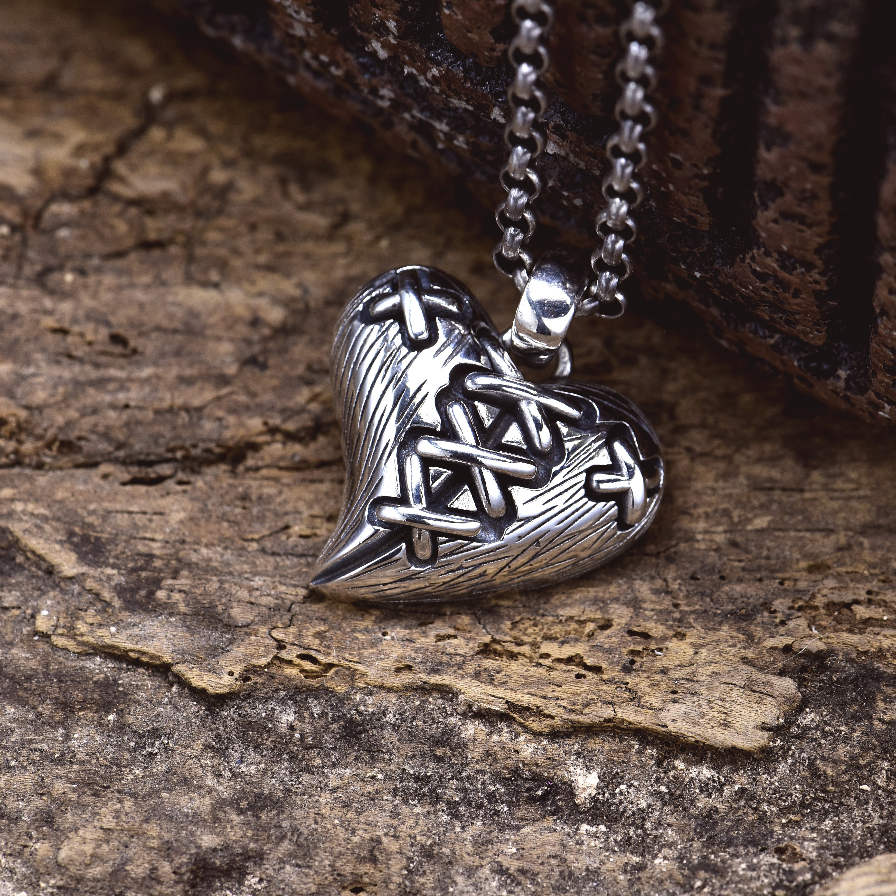 S925 stitched broken heart pendant on wood surface showing dimensional cross-stitch pattern and oxidized texture