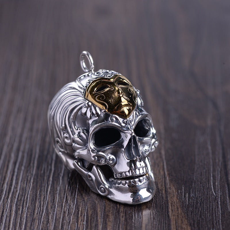 Pendant shown upright on a wooden surface, highlighting the hollow eyes, intricate side engravings, and gold detail across the skull cap.