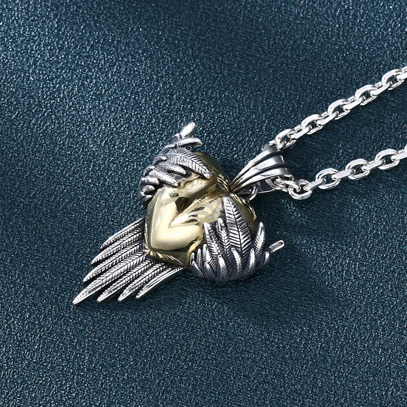 S925 sterling silver angel wing heart pendant on blue surface showing feather detailing, brass heart, and fringe chain accents