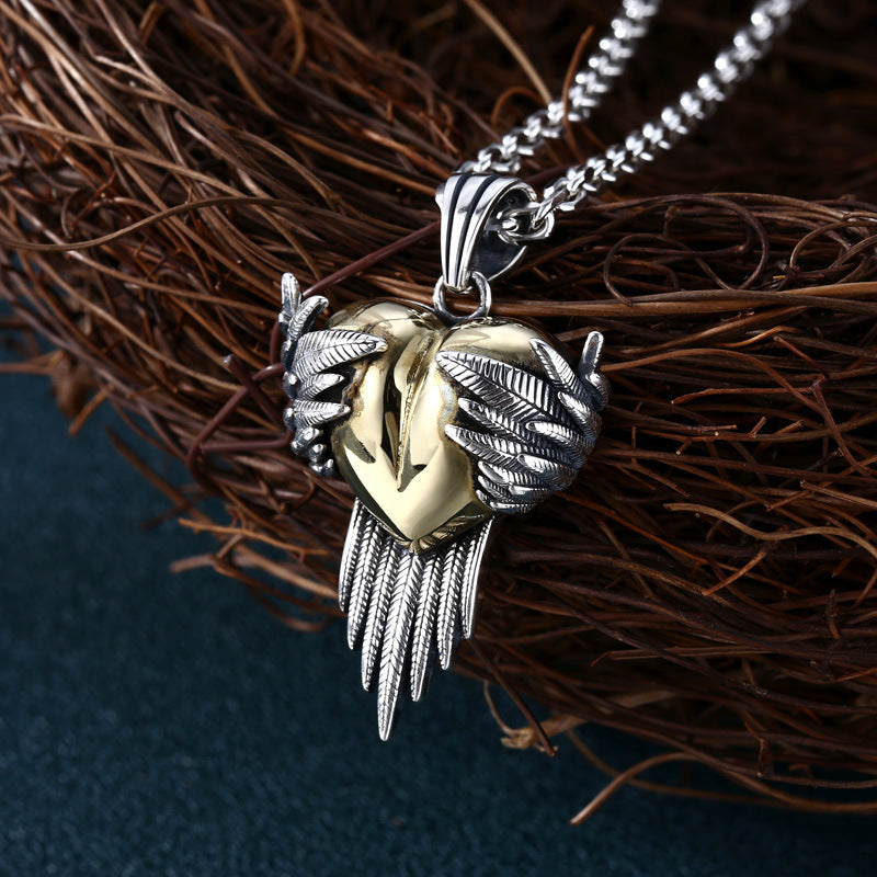 S925 sterling silver winged heart pendant on wood showing dimensional wing texture, brass heart accent, and oxidized finish