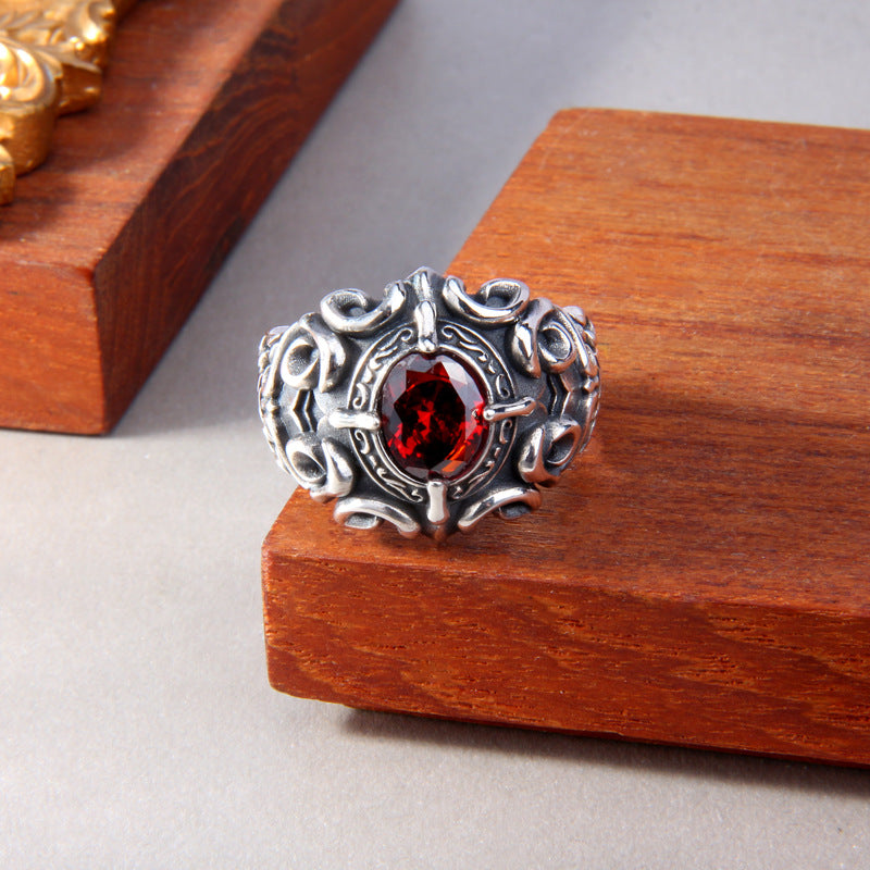 S925 sterling silver baroque ring on wooden surface showing faceted red zircon, dimensional scrollwork and gothic ornamental design