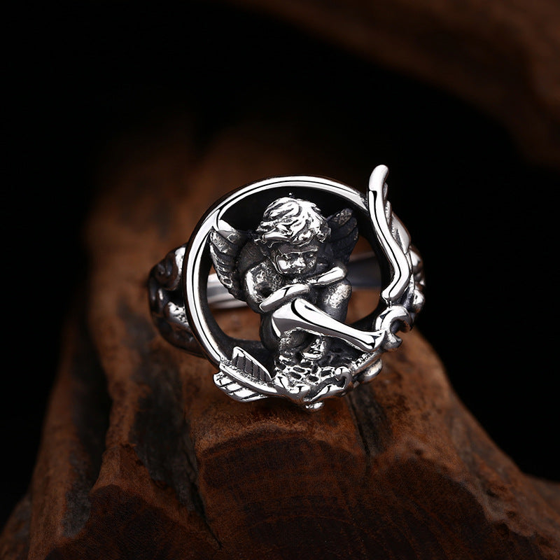 S925 sterling silver cupid ring on dark surface showing dimensional angel figure, black enamel contrast and oxidized detailing
