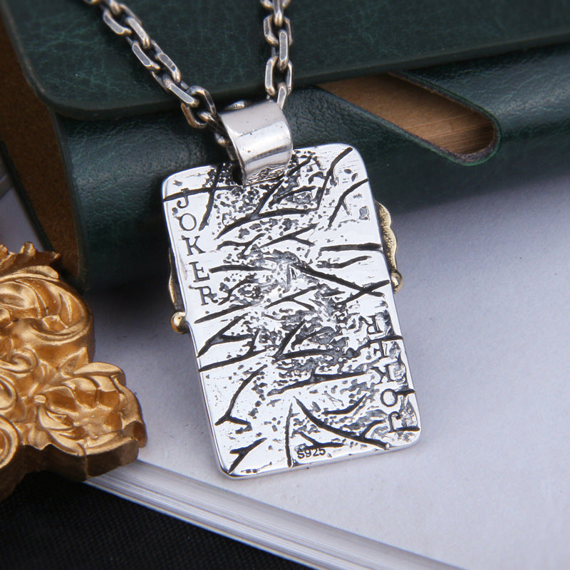Back view of S925 sterling silver joker pendant on dark surface showing reverse side brass accents and oxidized finish craftsmanship