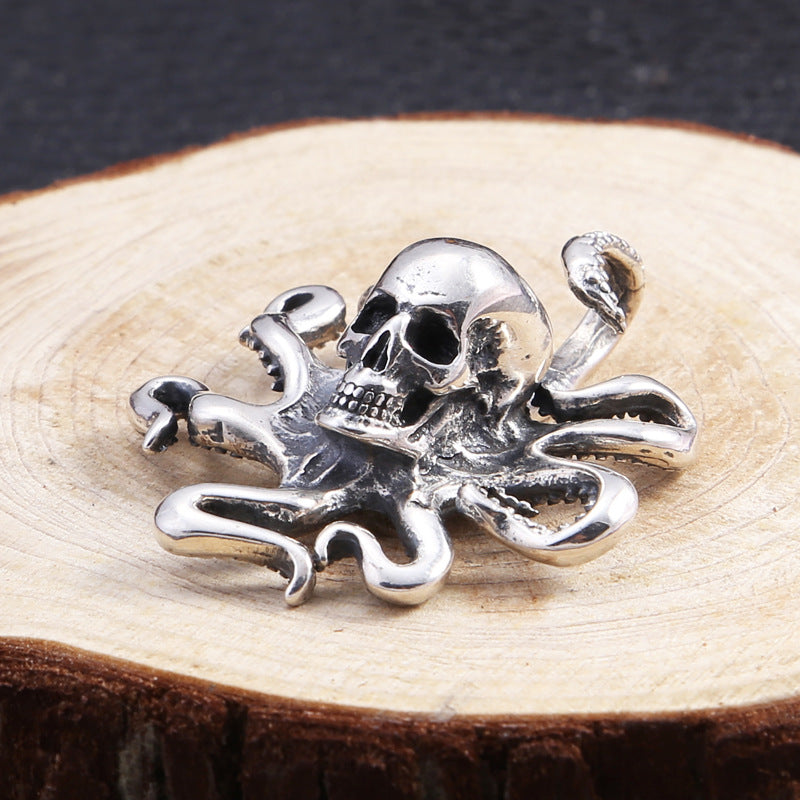 Pendant placed flat on a wooden surface with full view of the skull and extended tentacles in polished silver finish.