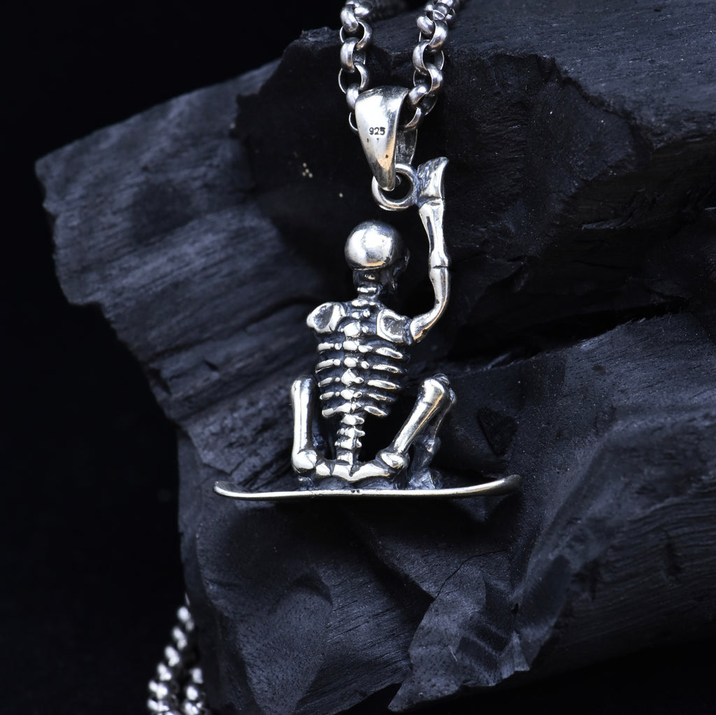 Sterling silver skeleton snowboarder pendant back view on dark stone showing 925 hallmark stamp and spine detail