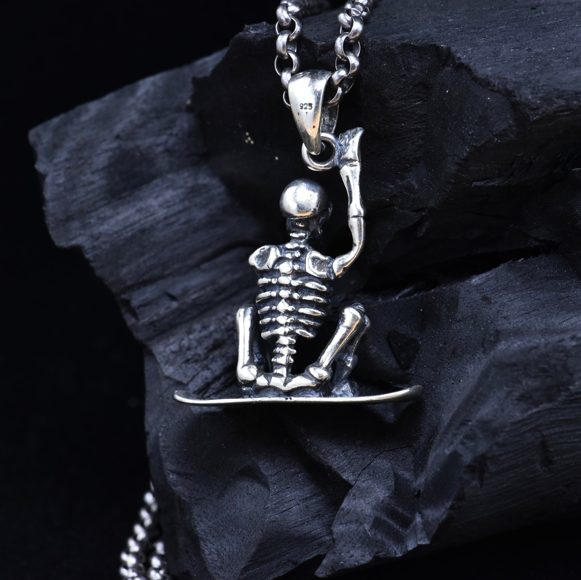 Sterling silver skeleton snowboarder pendant back view on dark stone showing 925 hallmark stamp and spine detail
