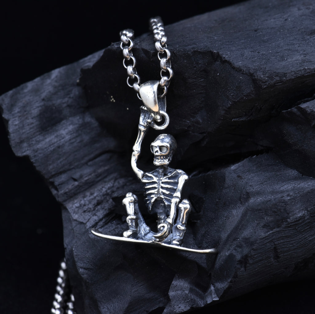 Sterling silver skeleton snowboarder pendant with chain on dark stone showing dimensional detail and oxidized finish