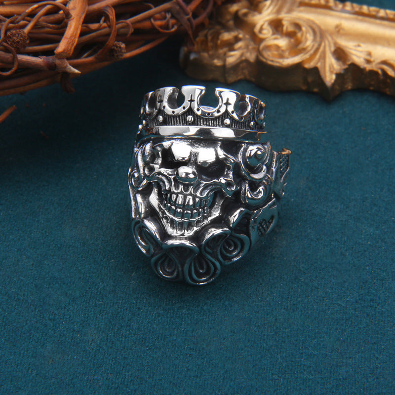 Sterling silver Gothic skull king ring on teal surface showing detailed crown, rose accents and dimensional skull relief