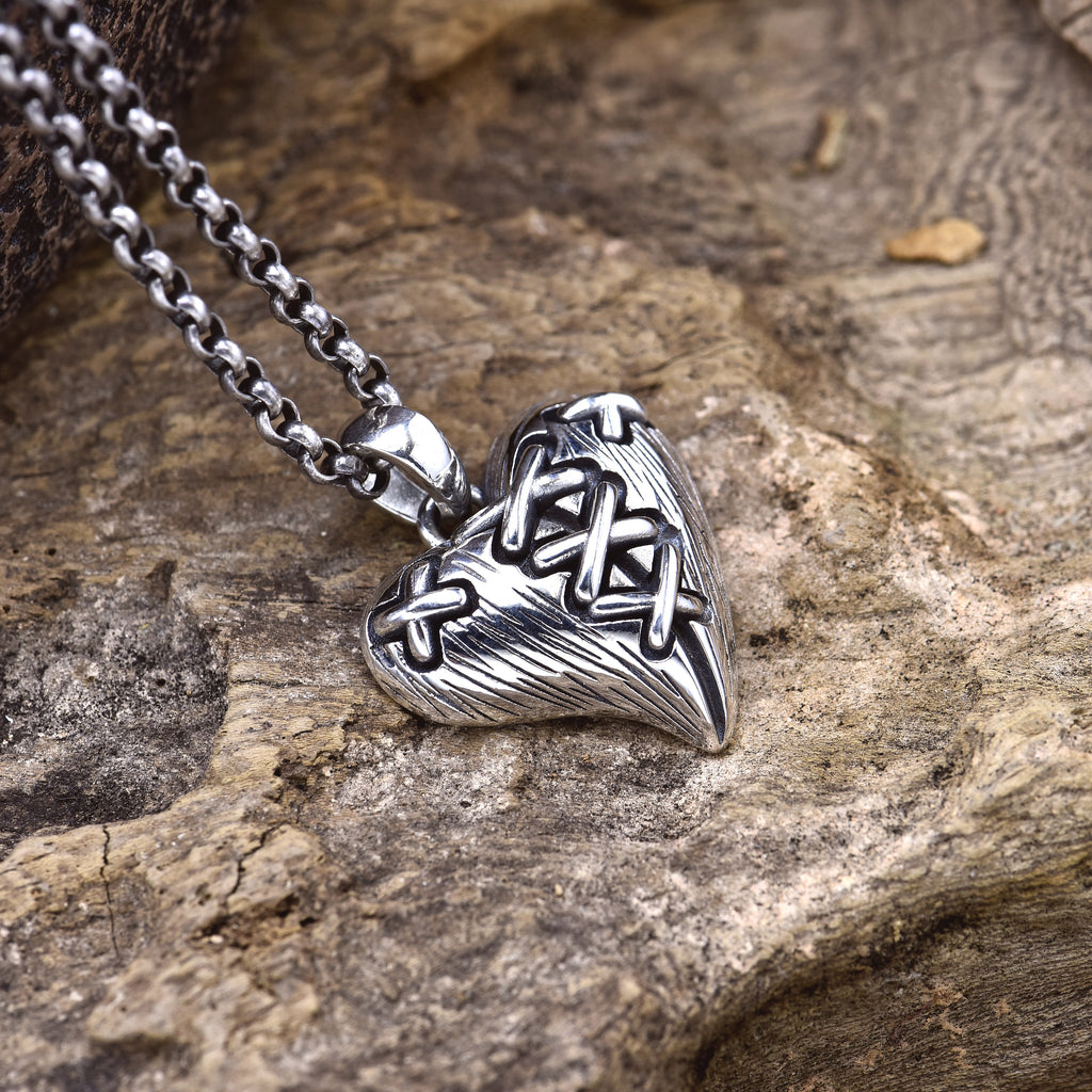 Sterling silver stitched broken heart pendant on wood surface showing cross-stitch detail and chain