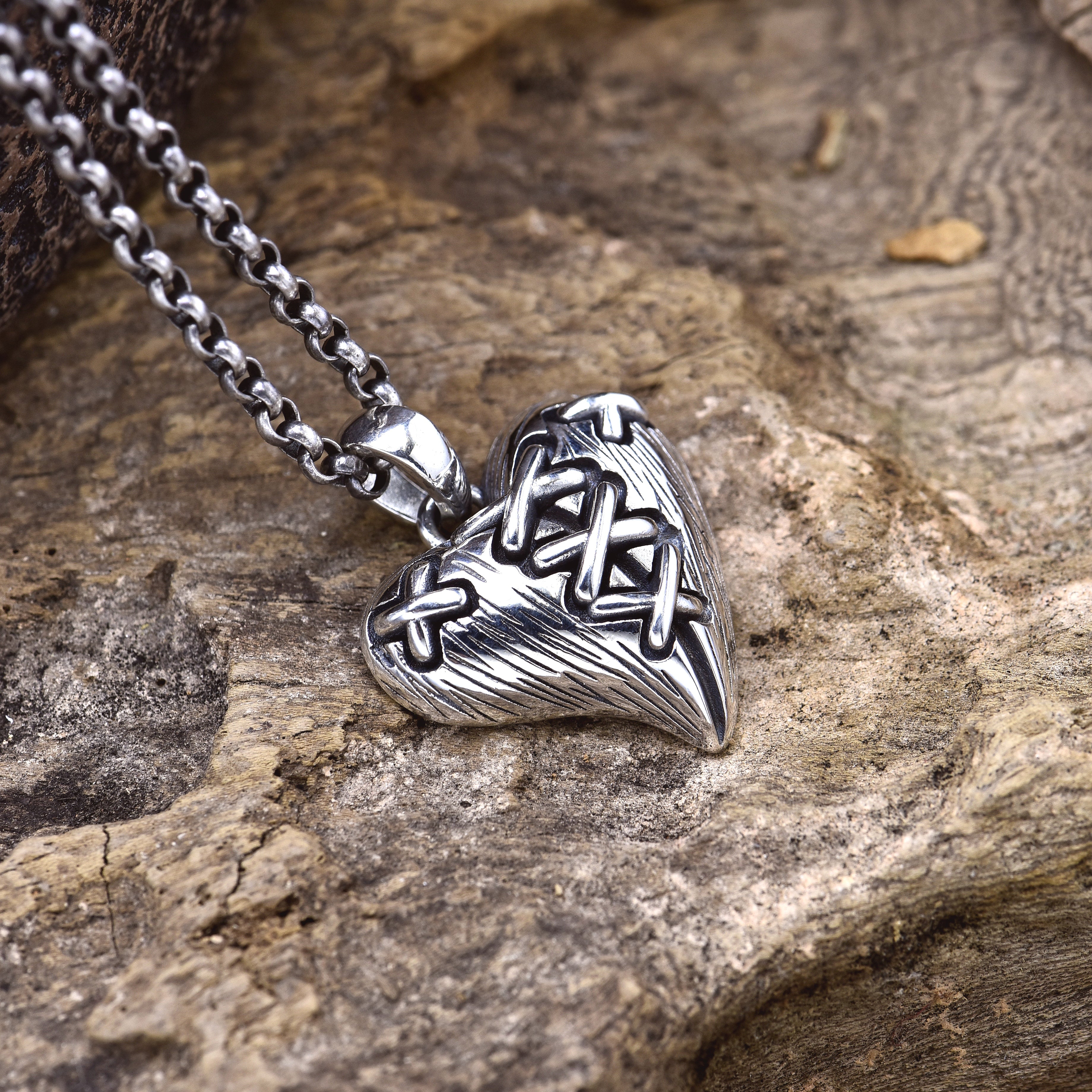 Sterling silver stitched broken heart pendant on wood surface showing cross-stitch detail and chain