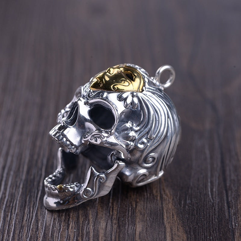 Flat surface shot displaying the skull pendant from a low angle, showing open jaw detailing and textured metallic hair-like engravings.